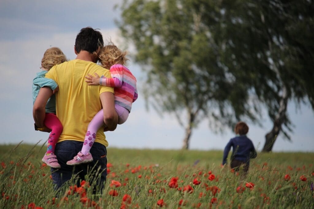 Father's Day, man carrying to girls on field of red petaled flower